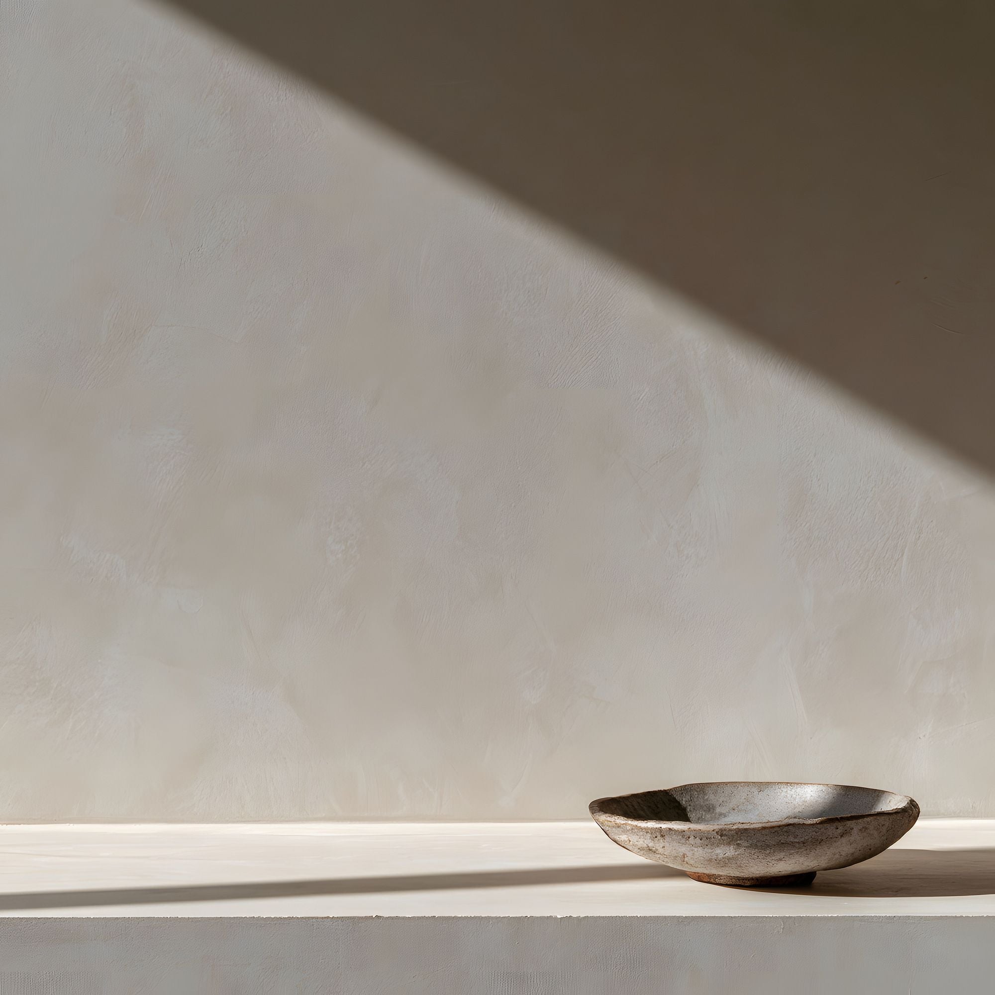 Quiet Objects No. 09 minimal still life artwork with a shallow dark stone bowl set against a softly textured cream wall with strong diagonal light and shadow.